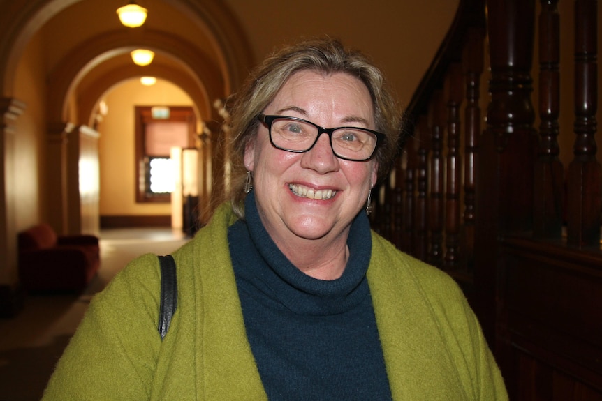 A woman wearing glasses and a green cardigan, smiling.