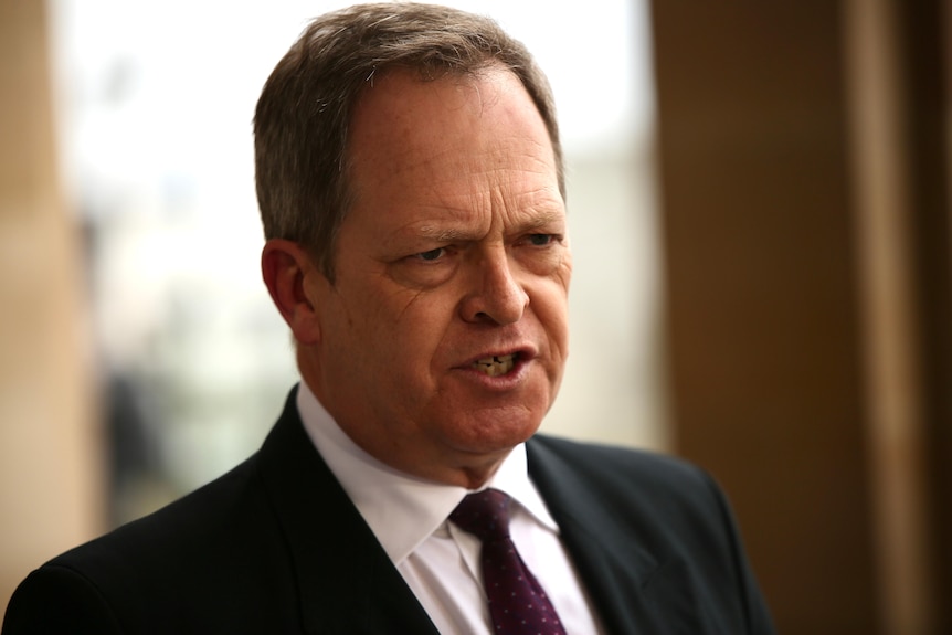 A man in a black suit speaks at a press conference