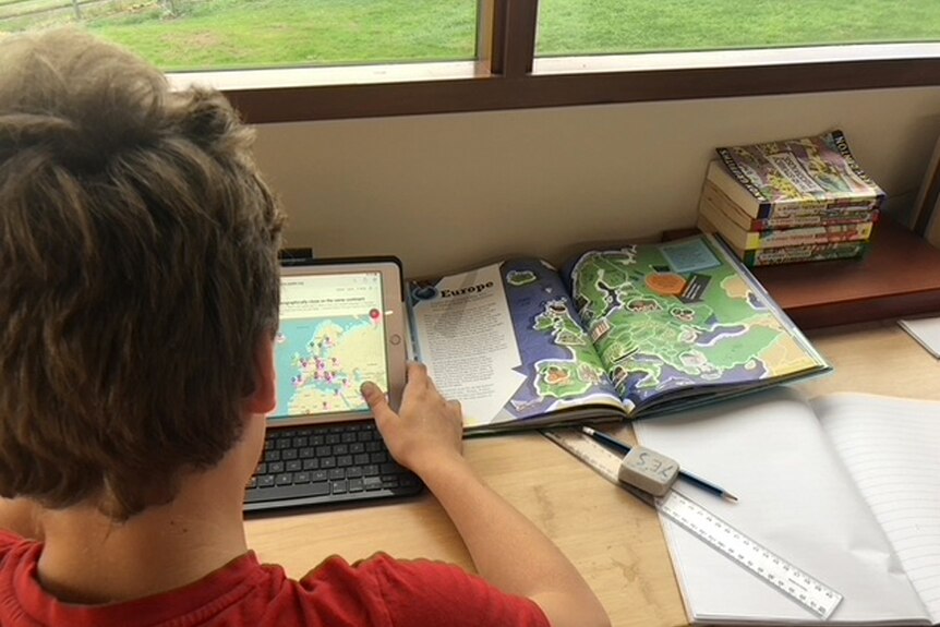 A photo of a young boy using an ipad at a desk overlooking a garden.