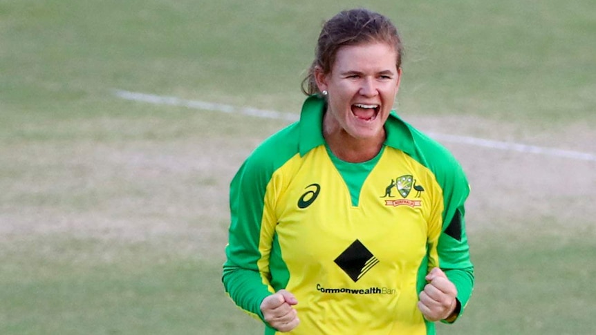 Jess Jonassen smiles and celebrates by clenching her hands wearing a yellow cricket kit