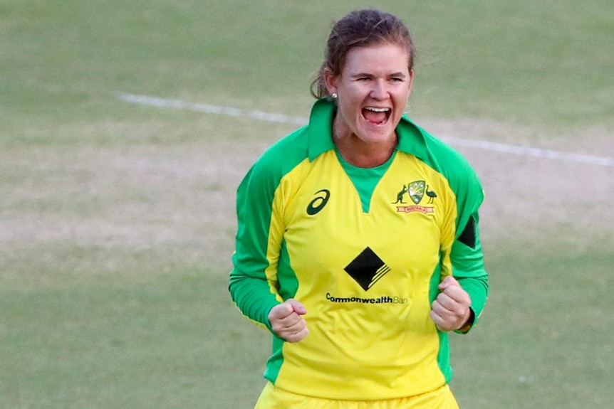 Jess Jonassen smiles and celebrates by clenching her hands wearing a yellow cricket kit