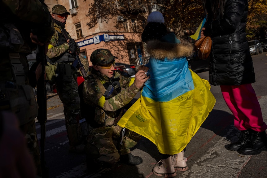 A soldier signs a Ukraine flag draped around a child