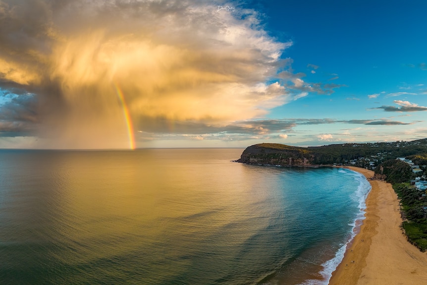 Sun-drenched cloud with rainbow rests just off shore