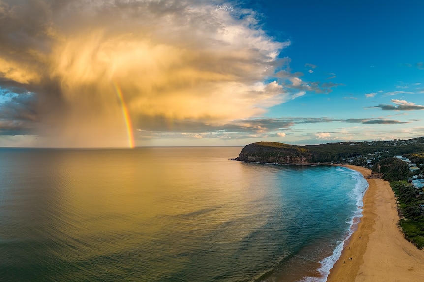 Sun-drenched cloud with rainbow rests just off shore.