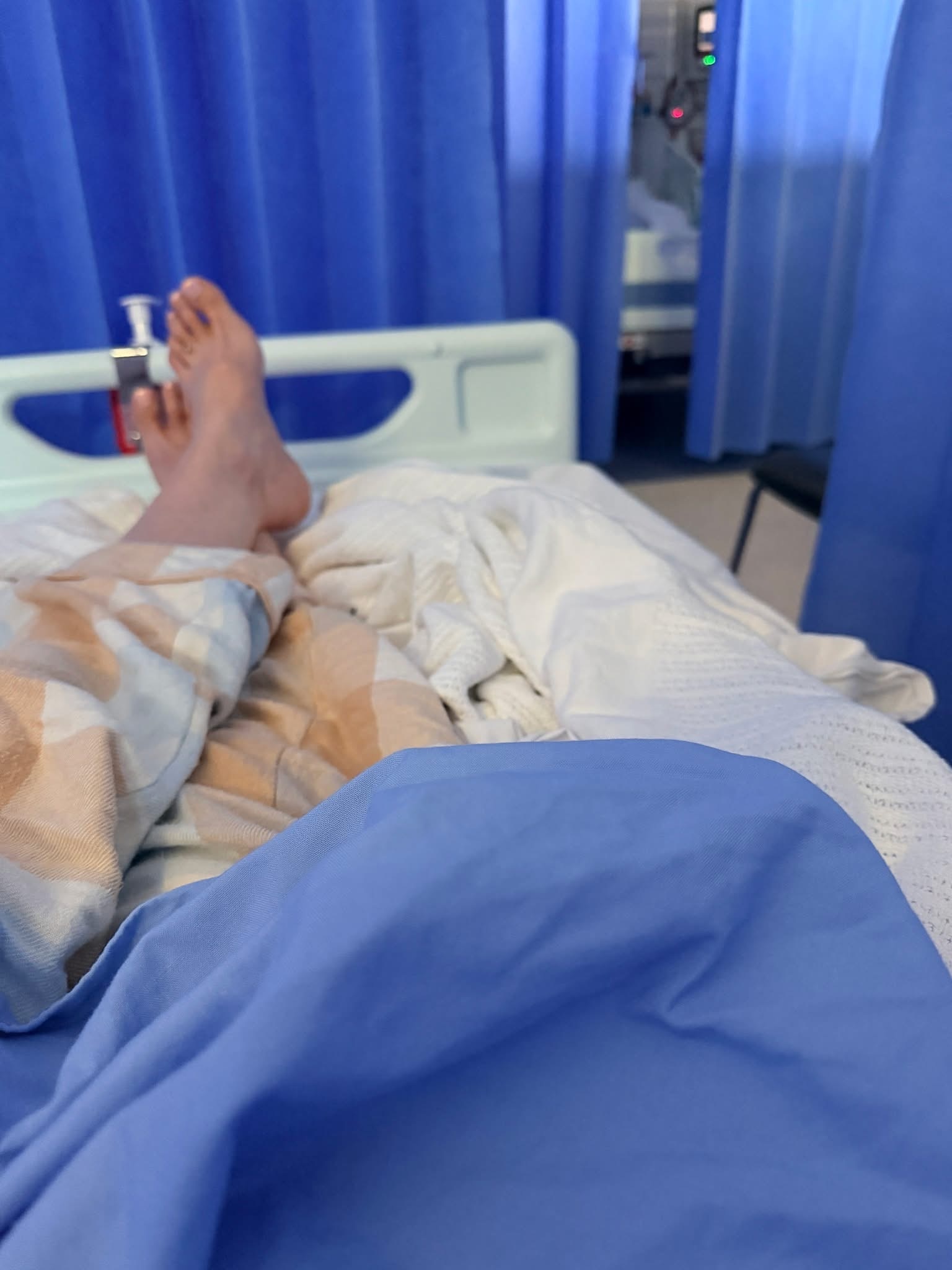 Pernas e pés numa cama de hospital, rodeados por uma cortina azul.