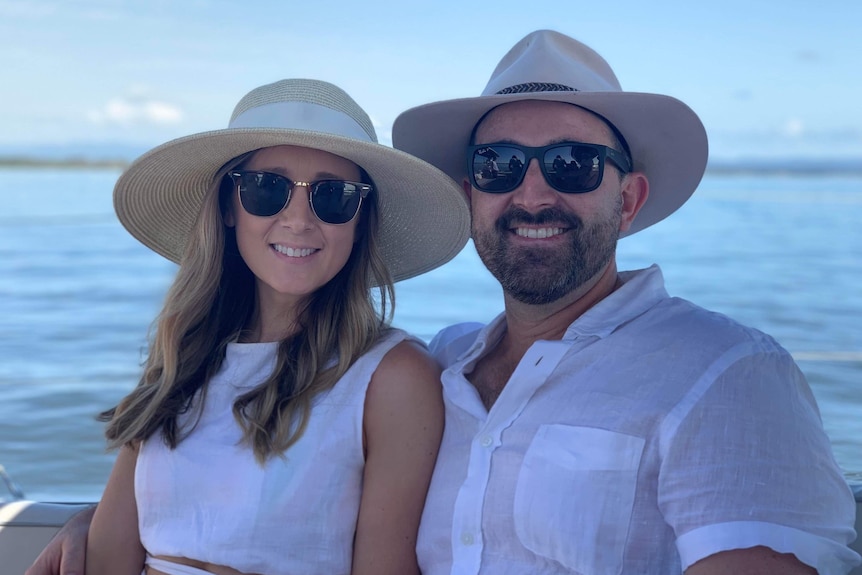 Young couple wearing hats and sunglasses smile on a boat.