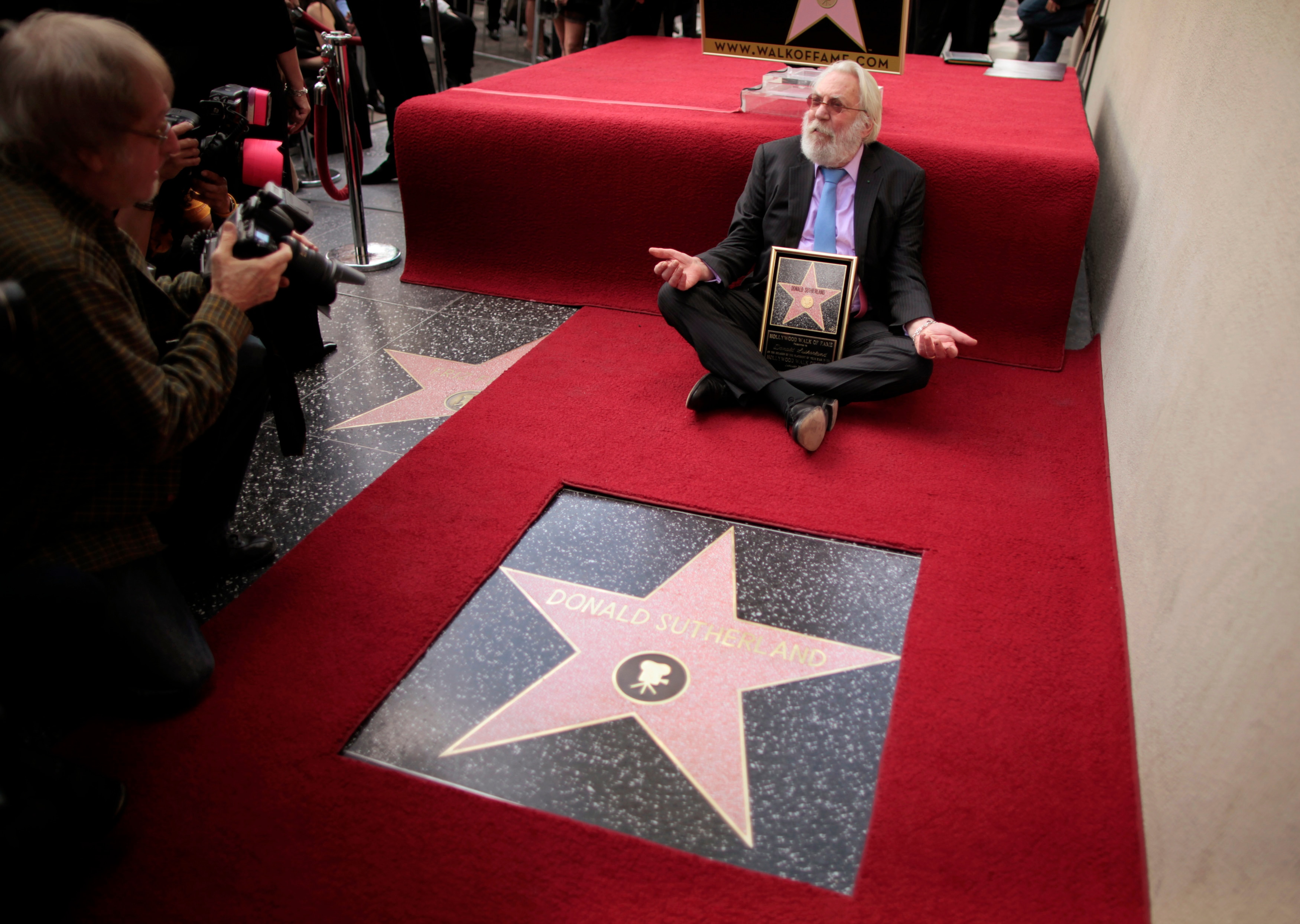 Actor Donald Sutherland sitting on the ground next to his hollywood star on the walk of fame