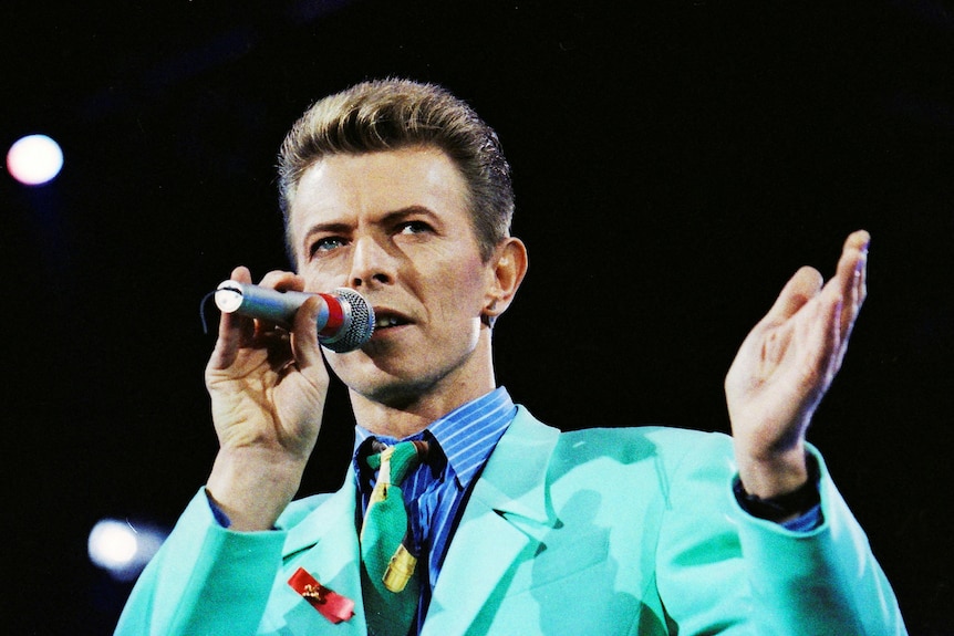 Man in blazer holding up microphone and singing at a concert