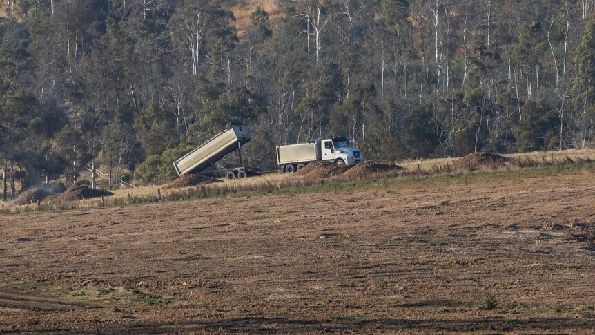 A truck dumping stuff on ground at farm. 