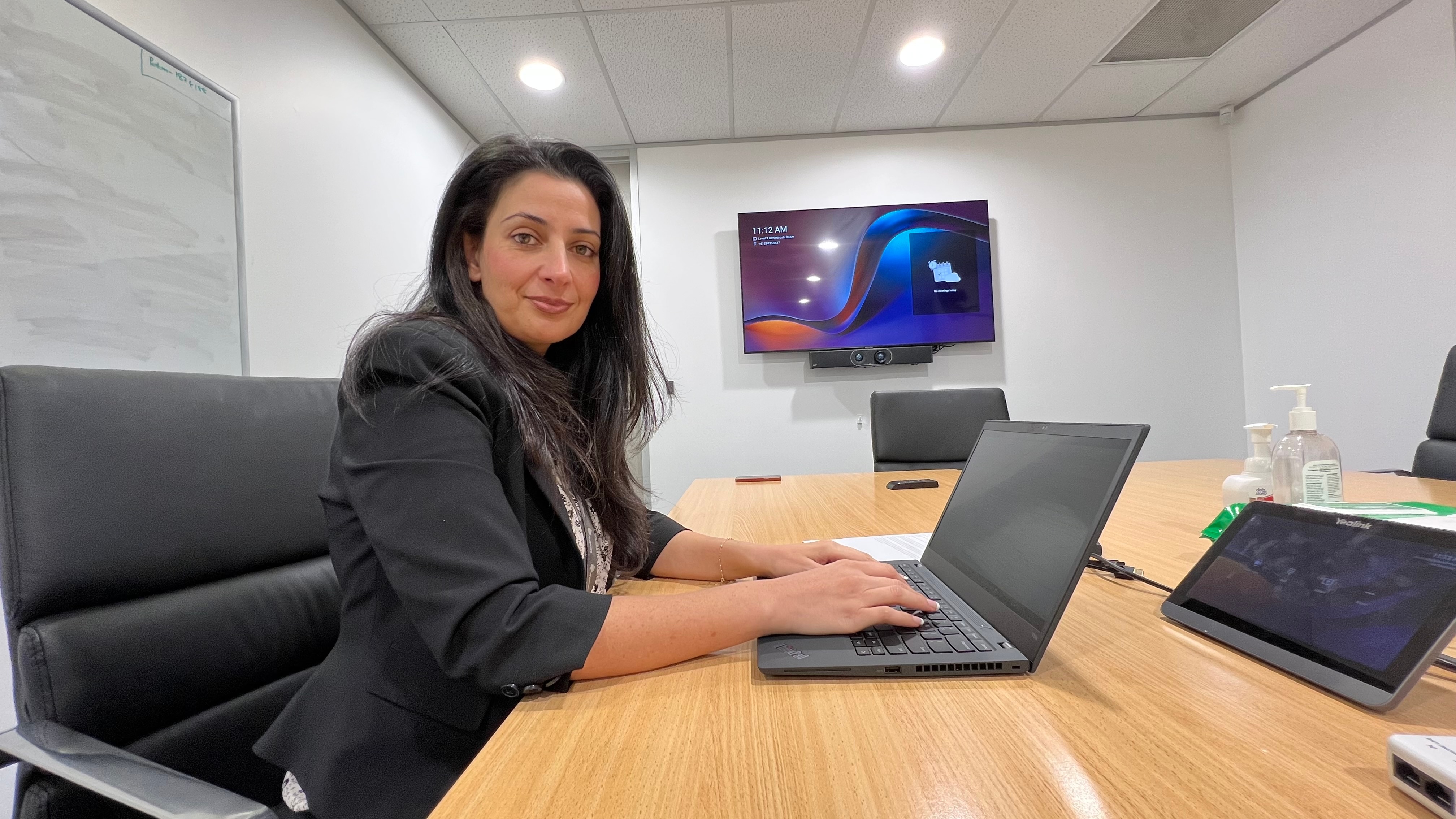 A woman in a suit sitting at a desk typing into a laptop