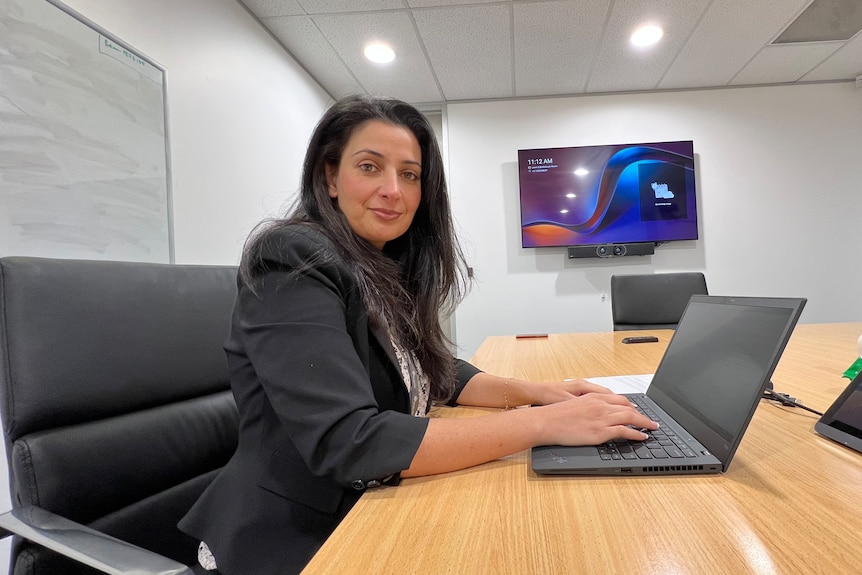 A woman in a suit sitting at a desk typing into a laptop