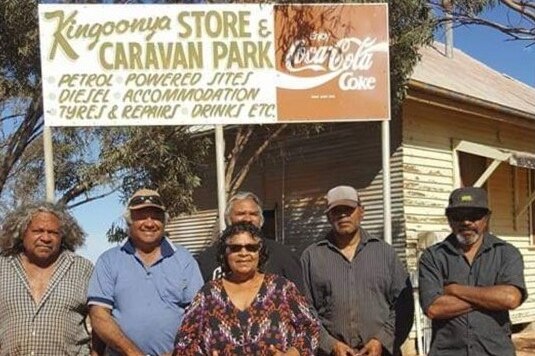 Five Aboriginal men and one Aboriginal woman stand in front of a sign advertising the Kingoonya store.