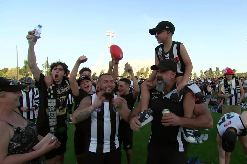 A boy on his father's shoulders. Everyone is dressed in Collingwood gear.