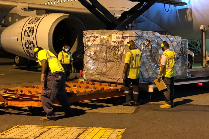공항 직원들이 항공기에서 Australian Aid가 표시된 화물을 내리고 있습니다.