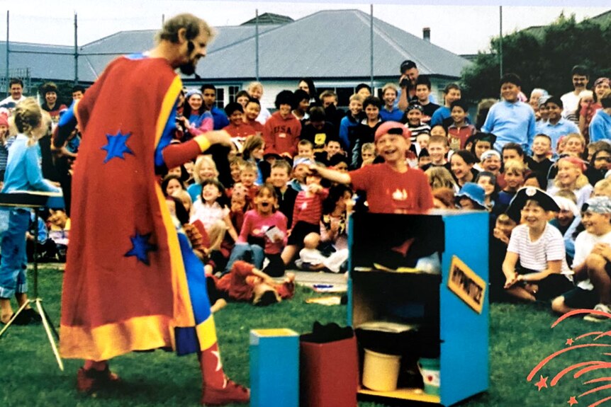 A man wearing a super suit performs magic tricks in front of kids. 