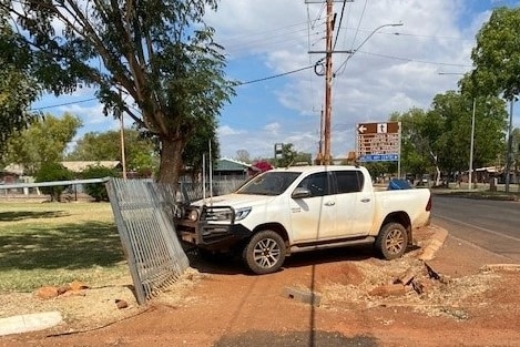 A white ute on an angle on the footpath against a mental fence