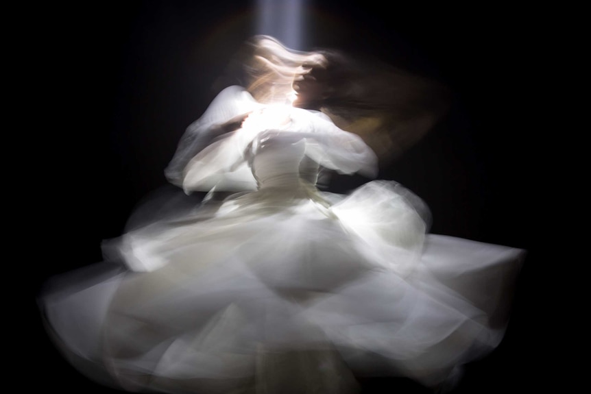 A figure in a white dress is captured in slow shutter speed, blurring the lines.