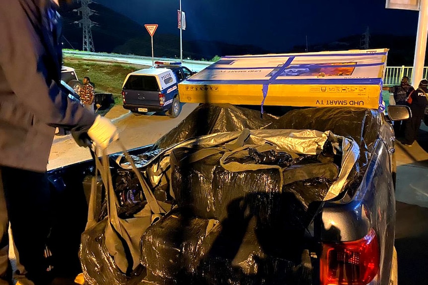 Heavy packages in plastic bags being loaded onto the back of a ute