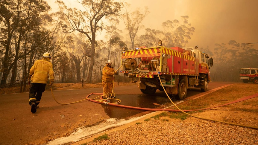 Two firefighters walk around a truck.