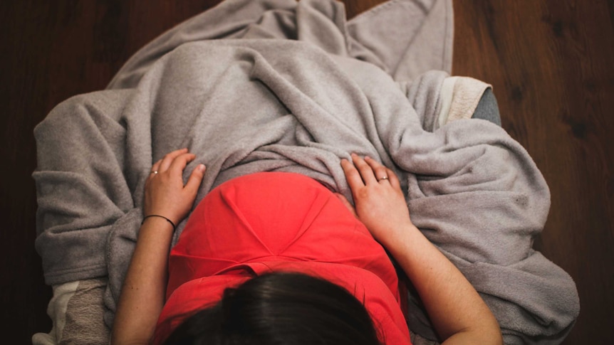 Woman looking down at her pregnant belly covered in a grey blanket