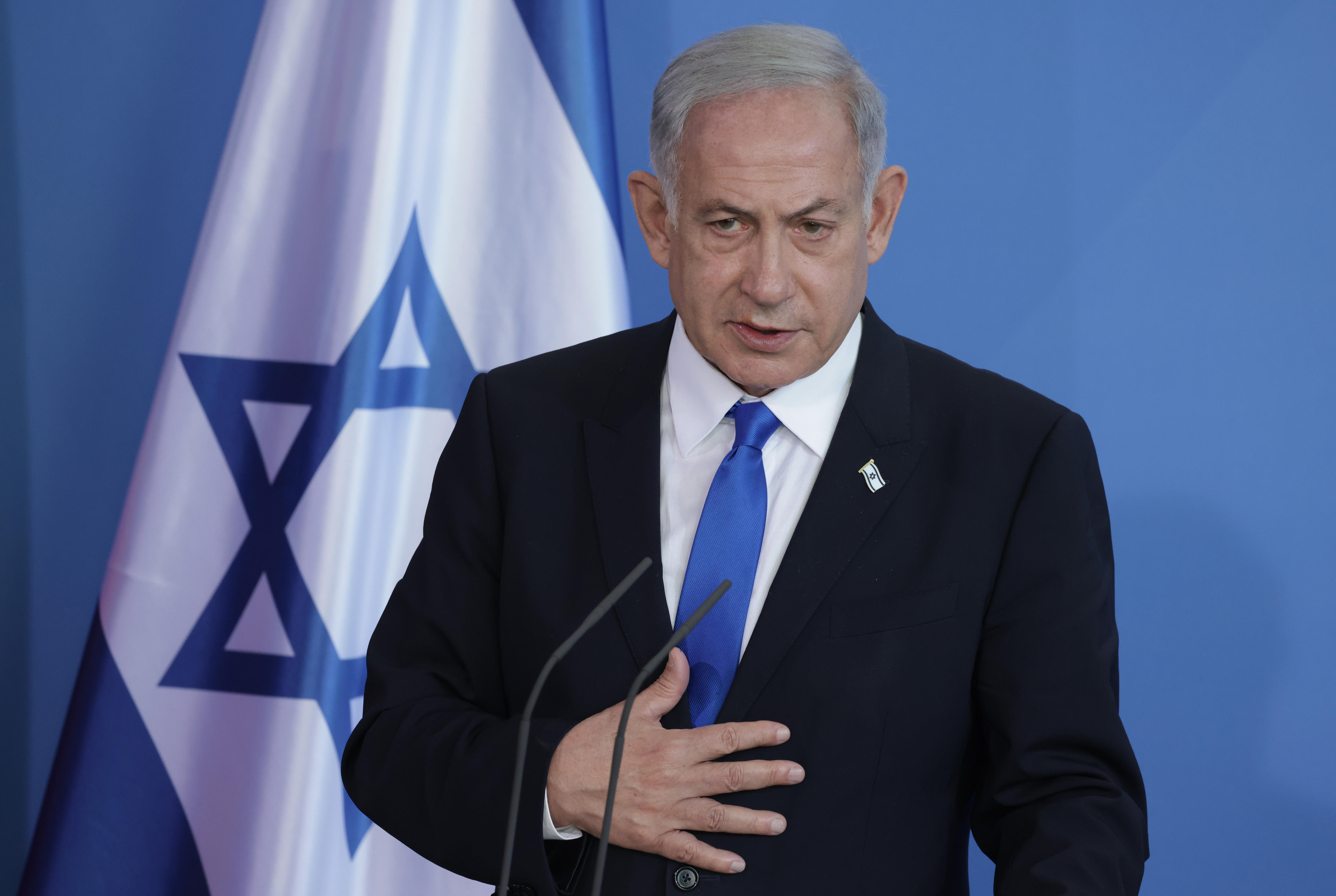 Benjamin Netanyahu wearing suit stands in front of flag of Israel