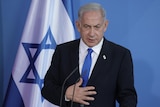 Benjamin Netanyahu wearing suit stands in front of flag of Israel