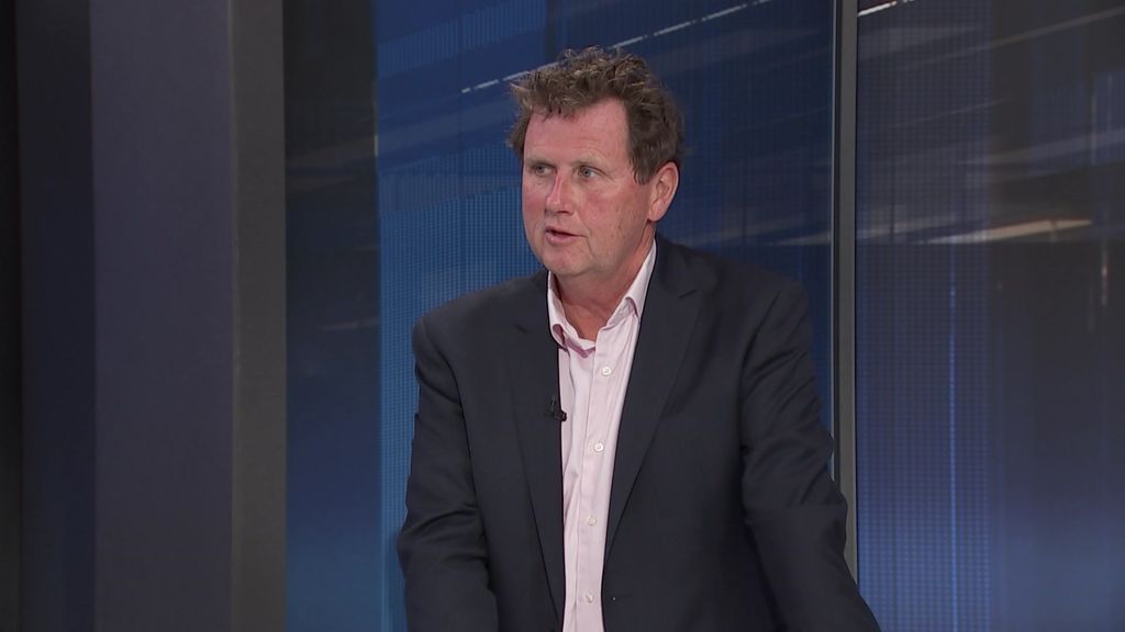A man with a dark suit jacket speaking in a television studio.