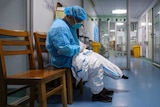 A doctor sits on a chair and puts on a quarantine suit