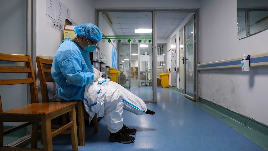 A doctor sits on a chair and puts on a quarantine suit