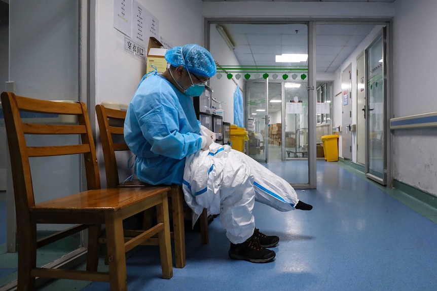 A doctor sits on a chair and puts on a quarantine suit