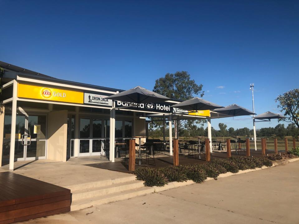 Single-storey hotel with garden, bushes and beer brand signage. 