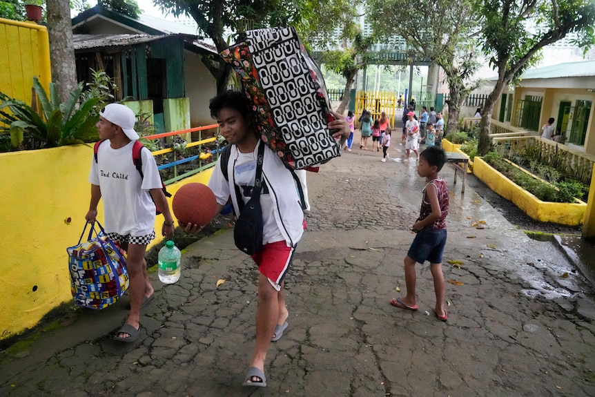Evacuees carry their belongings as they arrive at a temporary relocation site.