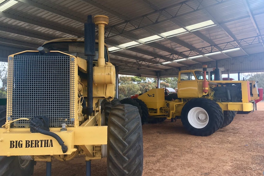 Close up shot of home built large yellow tractor made from truck parts with several other tractors in background