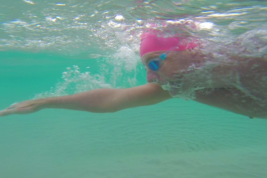 An underwater photo of a man in a pink swimming cap and goggles swimming at the beach