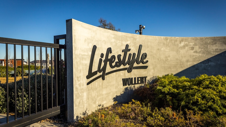 The black metal gate of a housing estate with the words "Lifestyle Wollert" on a wall.