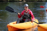 A woman kayaks on a river smiling at the camera.