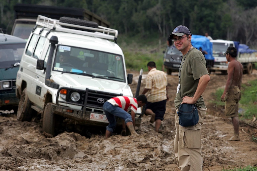 Dean Yates stands in front of a bogged car in Indonesia.