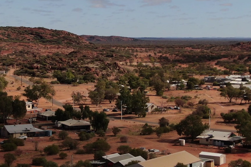 An aerial shot of a small desert town with red dirt trailing off into the distance