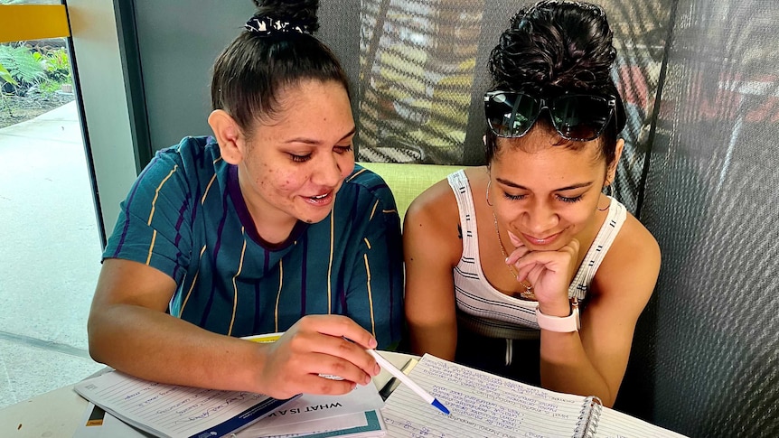 Two young Indigenous girls sit with study books in front of them.