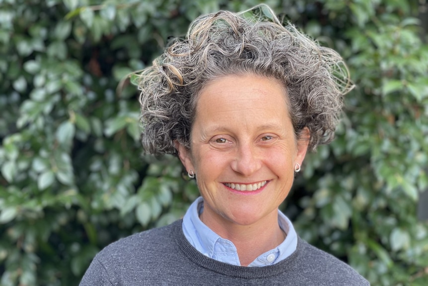 A woman with curly grey short hair smiles at the camera. 