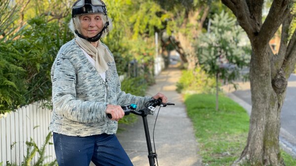 A woman with white hair, grey cardigan and a helmet on an e-scooter