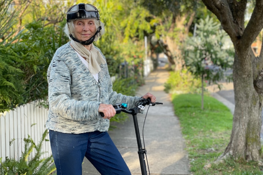 A woman with white hair, grey cardigan and a helmet on an e-scooter