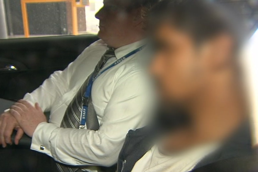 A blurred image of a the suspect arrested over Aiia Maasarwe's death, sitting beside a detective in the back of a car.