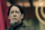 Ann Dowd holds a microphone with a pained look on her face.