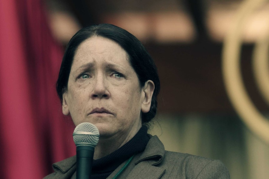 Ann Dowd holds a microphone with a pained look on her face.