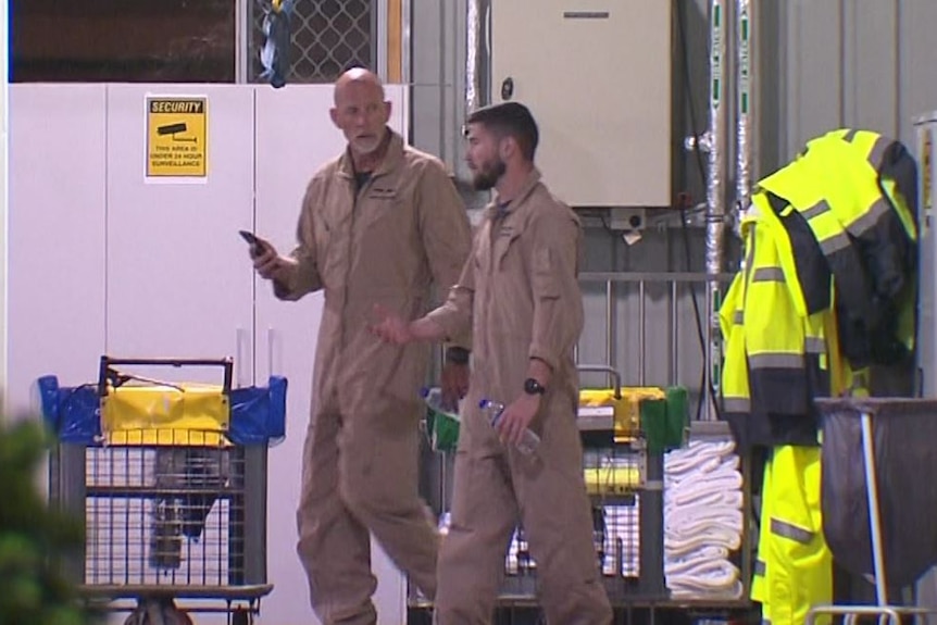 Two men wearing air suits walking outside chatting to each other. 