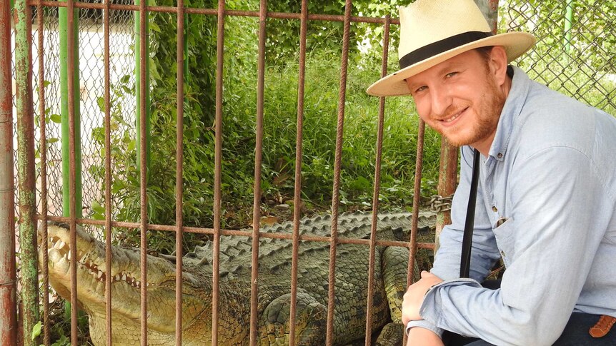 Sebastian Brackhane stands next to a crocodile in an enclosure