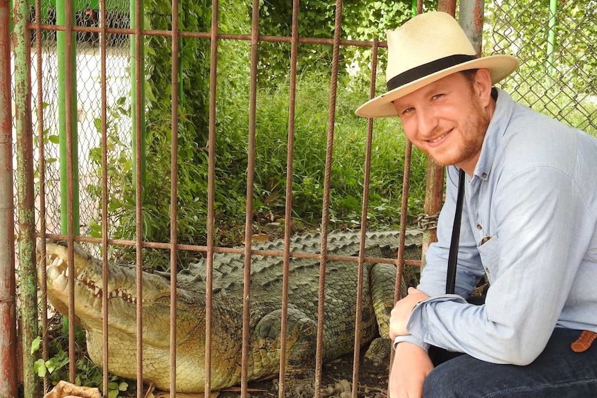 Sebastian Brackhane stands next to a crocodile in an enclosure