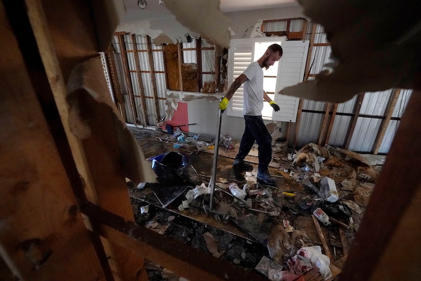 Un hombre sostiene una herramienta mientras camina por una casa destruida por un huracán. 