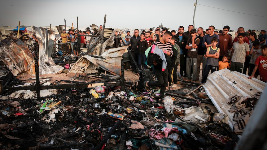 Palestinians look at burnt buildings and debris after an Israeli strike.